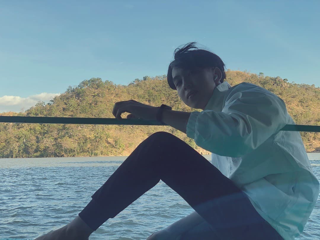 Duy sitting by the water with mountains in the distance
